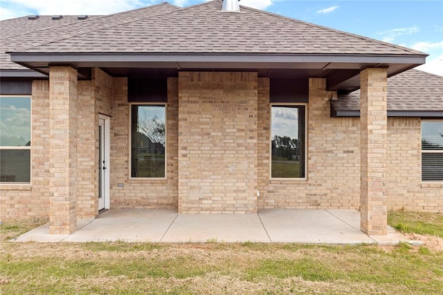 view of exterior entry with roof with shingles and a patio