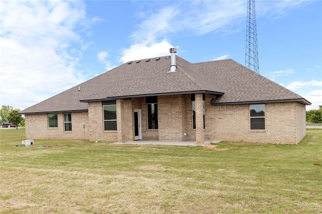 back of house with roof with shingles, brick siding, a patio area, and a yard