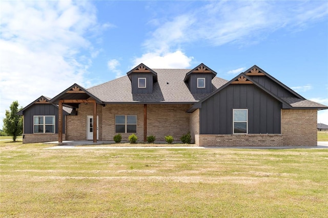 view of front of property featuring board and batten siding, brick siding, a front yard, and roof with shingles