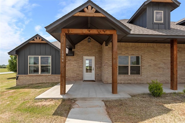 doorway to property featuring board and batten siding, a patio, and brick siding