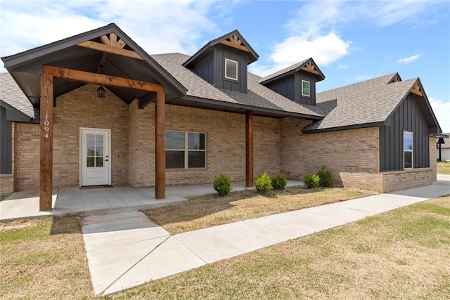 view of front of house featuring brick siding, a front yard, board and batten siding, and a shingled roof