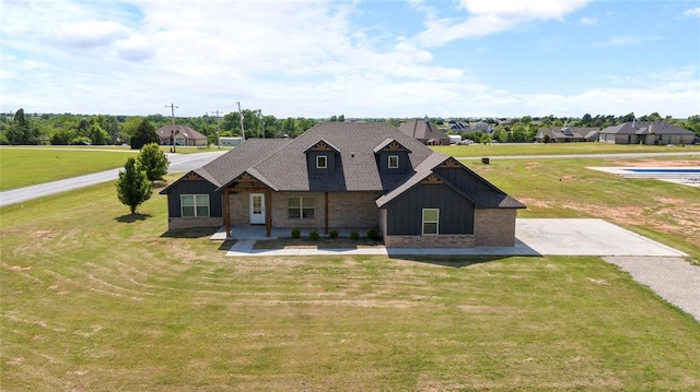 view of front of property with board and batten siding, a front yard, brick siding, and roof with shingles