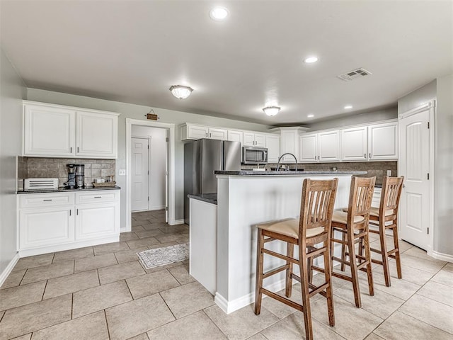 kitchen featuring appliances with stainless steel finishes, tasteful backsplash, dark countertops, baseboards, and a breakfast bar area