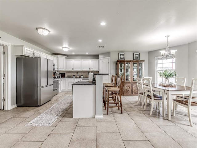 kitchen with appliances with stainless steel finishes, dark countertops, white cabinetry, a chandelier, and backsplash