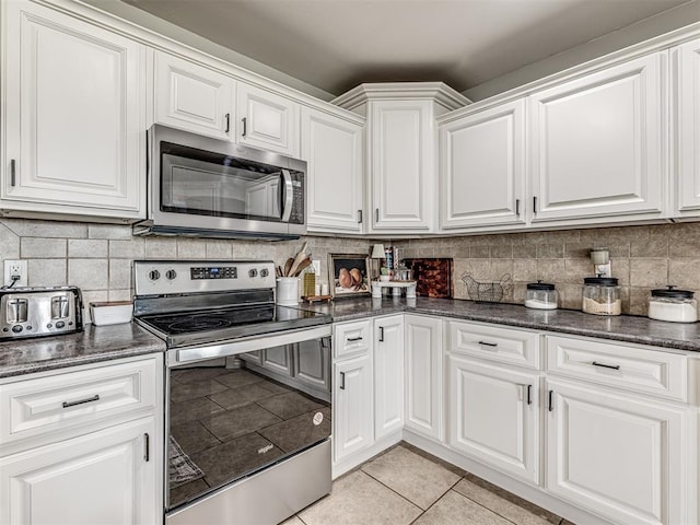 kitchen featuring stainless steel appliances, light tile patterned floors, white cabinetry, tasteful backsplash, and dark stone counters