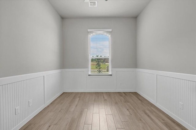 empty room featuring light wood-style floors and a wainscoted wall