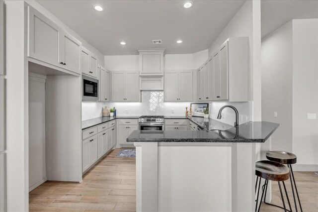 kitchen featuring built in microwave, a sink, a peninsula, stainless steel gas range oven, and light wood-style floors