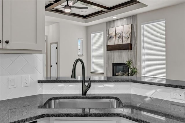kitchen featuring ceiling fan, a large fireplace, white cabinets, a sink, and decorative backsplash