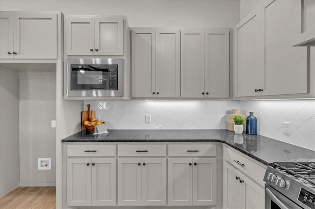 kitchen with stainless steel appliances, light wood finished floors, dark stone countertops, and decorative backsplash
