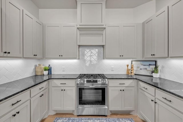 kitchen with stainless steel gas range oven, dark stone counters, light wood finished floors, and tasteful backsplash