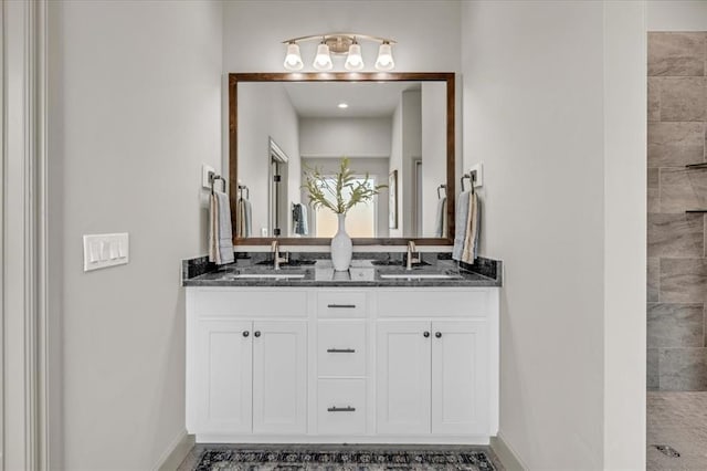 full bath with baseboards, double vanity, and tiled shower