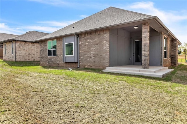 back of house with brick siding, roof with shingles, a lawn, and a patio area