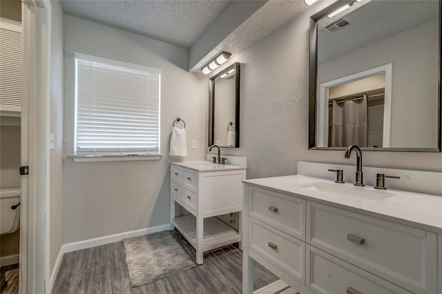 7301 Kings Manor Ct, Oklahoma City, OK 73132 - full bathroom featuring a textured ceiling, wood finished floors, two vanities, toilet, and baseboards