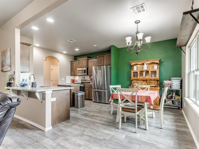 5702 Cedar Tree Cir, Guthrie, OK 73044 - kitchen with stainless steel appliances, a peninsula, a chandelier, light wood finished floors, and a kitchen bar