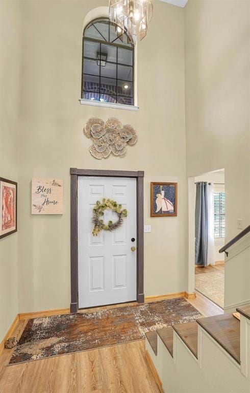 foyer entrance with a high ceiling, a chandelier, wood finished floors, baseboards, and stairs
