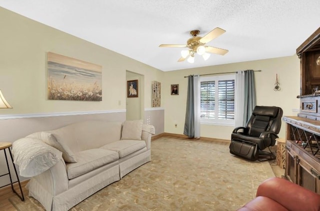 living room featuring ceiling fan, baseboards, and a textured ceiling