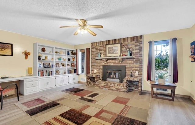 living area with wood finished floors, a ceiling fan, a textured ceiling, and a brick fireplace