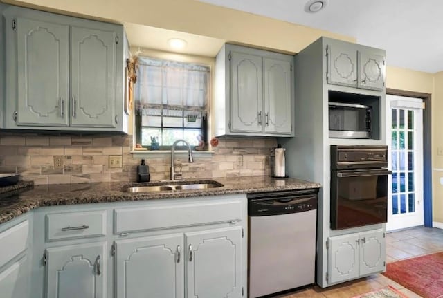 kitchen featuring appliances with stainless steel finishes, a sink, backsplash, and dark stone counters