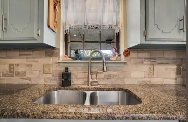 kitchen featuring a sink, dark stone counters, and backsplash
