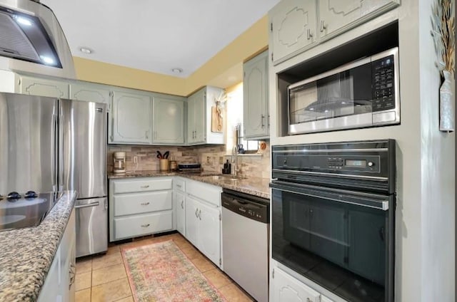 kitchen with black appliances, backsplash, light stone counters, light tile patterned floors, and a sink