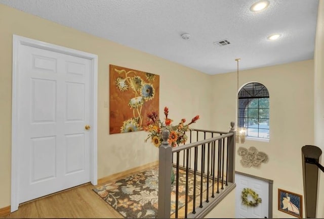 hallway featuring a textured ceiling, an upstairs landing, wood finished floors, baseboards, and recessed lighting