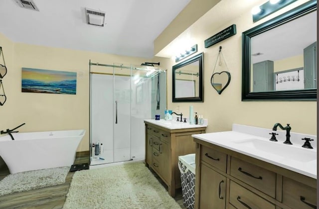 bathroom featuring a stall shower, two vanities, wood finished floors, and a freestanding bath