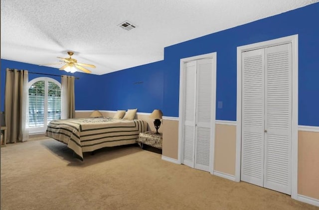 carpeted bedroom featuring multiple closets, a textured ceiling, ceiling fan, and baseboards