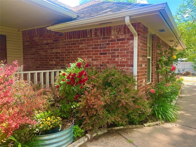 view of home's exterior with brick siding, fence, and a shingled roof