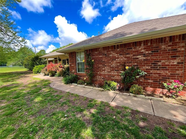 view of home's exterior featuring brick siding, a yard, and roof with shingles