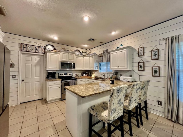 kitchen featuring appliances with stainless steel finishes, a peninsula, light tile patterned floors, a kitchen breakfast bar, and light stone counters