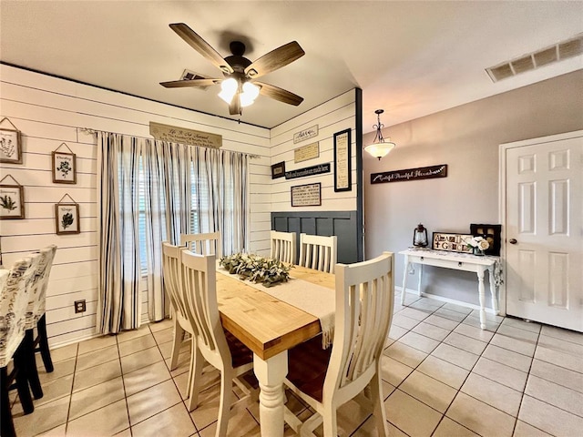 dining space with light tile patterned floors, ceiling fan, and wood walls