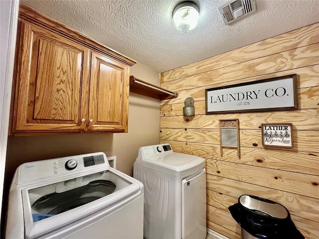 washroom with washing machine and clothes dryer, cabinet space, wood walls, and a textured ceiling
