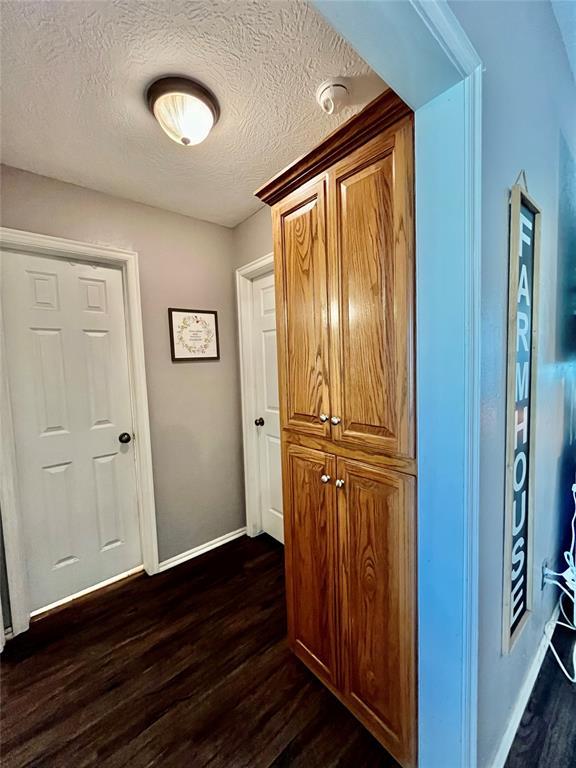 hall with dark wood-type flooring, baseboards, and a textured ceiling