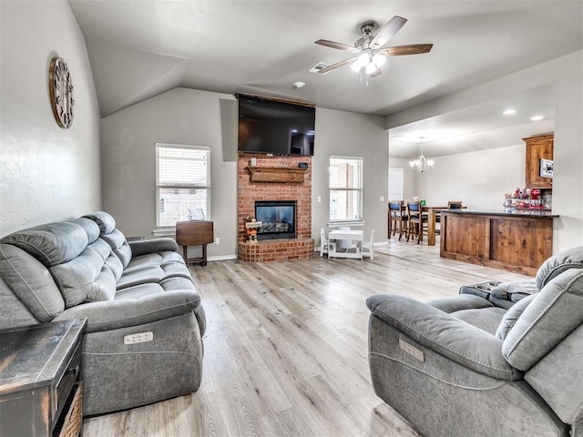 living area with ceiling fan, plenty of natural light, light wood finished floors, a brick fireplace, and vaulted ceiling