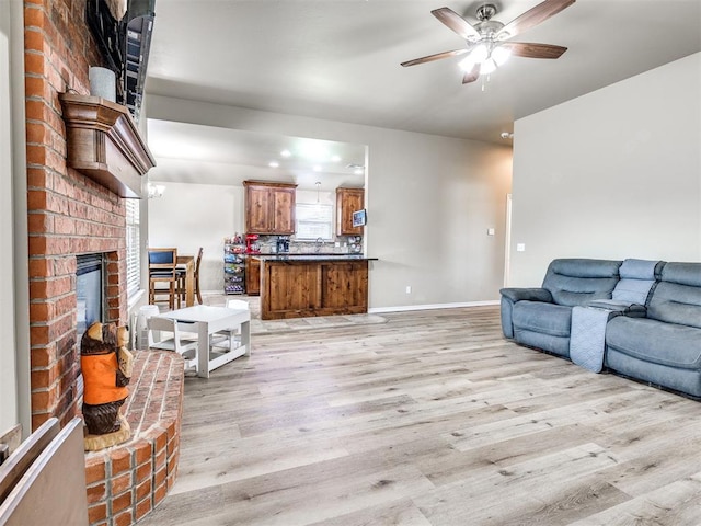 living area featuring light wood-style flooring, a ceiling fan, baseboards, and a fireplace