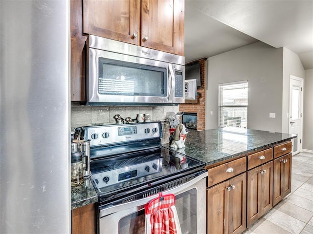 kitchen with appliances with stainless steel finishes, light tile patterned floors, dark stone countertops, brown cabinets, and decorative backsplash
