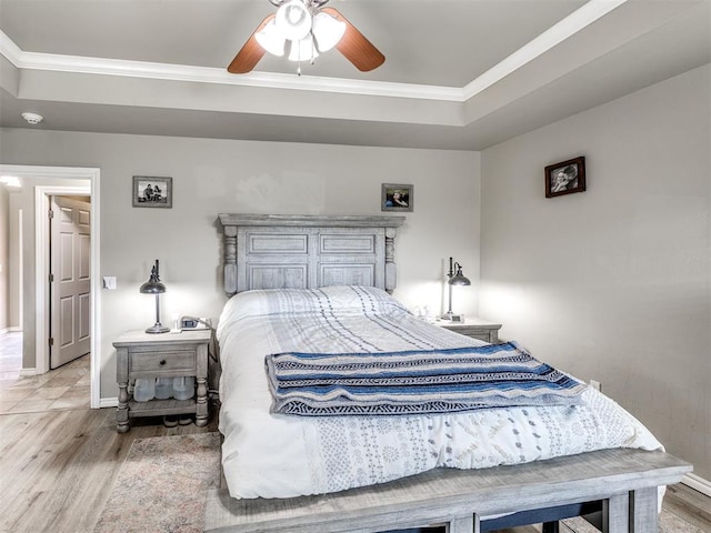 bedroom with wood finished floors, a tray ceiling, crown molding, and baseboards