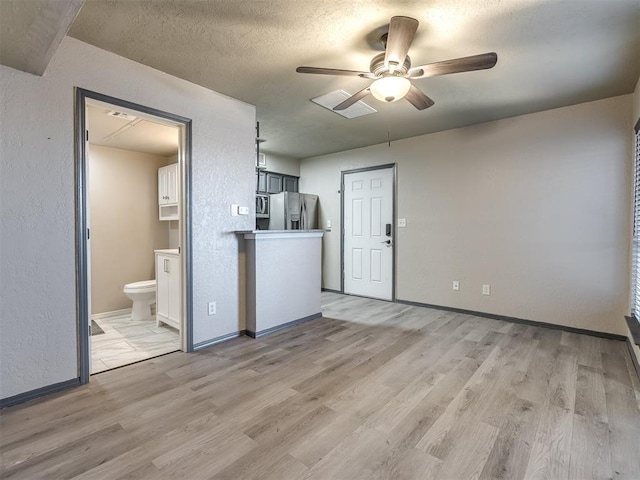 11530 N May Ave Unit D303, Oklahoma City, OK 73120 - unfurnished living room featuring a textured wall, ceiling fan, light wood-type flooring, baseboards, and a textured ceiling