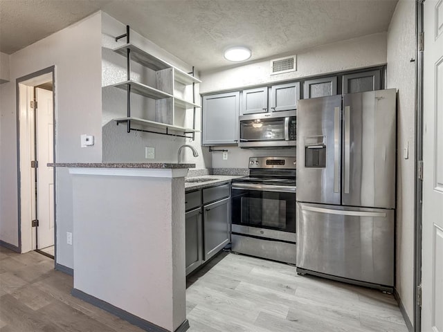 11530 N May Ave Unit D303, Oklahoma City, OK 73120 - kitchen featuring stainless steel appliances, light wood-type flooring, open shelves, gray cabinets, and a textured ceiling