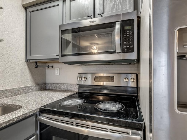 11530 N May Ave Unit D303, Oklahoma City, OK 73120 - kitchen featuring appliances with stainless steel finishes, gray cabinetry, and a textured wall