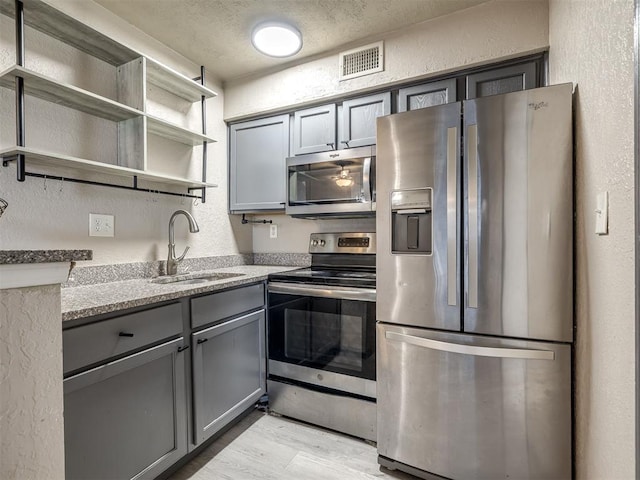 11530 N May Ave Unit D303, Oklahoma City, OK 73120 - kitchen with stainless steel appliances, gray cabinets, a textured wall, light wood finished floors, and light stone countertops