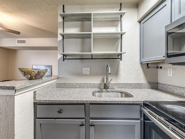 11530 N May Ave Unit D303, Oklahoma City, OK 73120 - kitchen with gray cabinets, open shelves, stainless steel microwave, and a textured wall