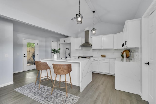 kitchen featuring wall chimney exhaust hood, lofted ceiling, a kitchen island with sink, white cabinetry, and a sink