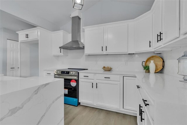 kitchen with stainless steel electric range, wall chimney exhaust hood, white cabinets, and vaulted ceiling