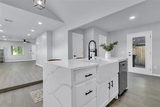 kitchen featuring stainless steel dishwasher, light wood-style floors, a sink, white cabinetry, and baseboards