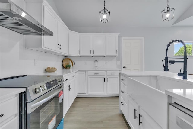 kitchen with stainless steel range with electric cooktop, wall chimney exhaust hood, a sink, white cabinets, and decorative light fixtures