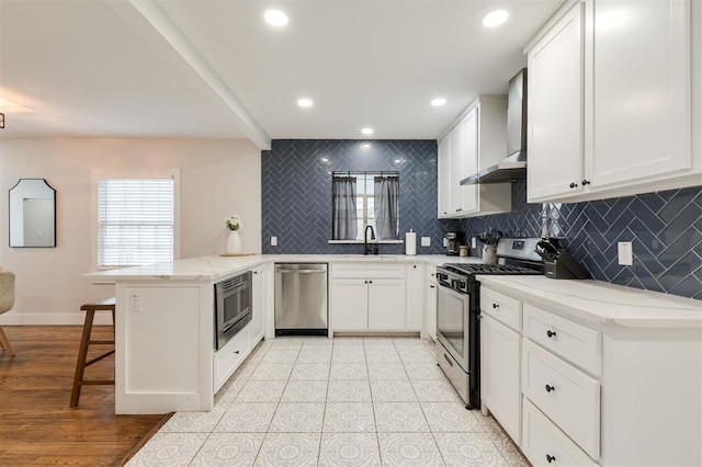 2237 NW 30th St, Oklahoma City, OK 73112 - kitchen featuring appliances with stainless steel finishes, wall chimney exhaust hood, a peninsula, decorative backsplash, and a kitchen breakfast bar