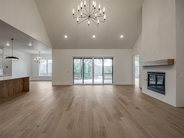 unfurnished living room with a chandelier, high vaulted ceiling, a glass covered fireplace, recessed lighting, and baseboards