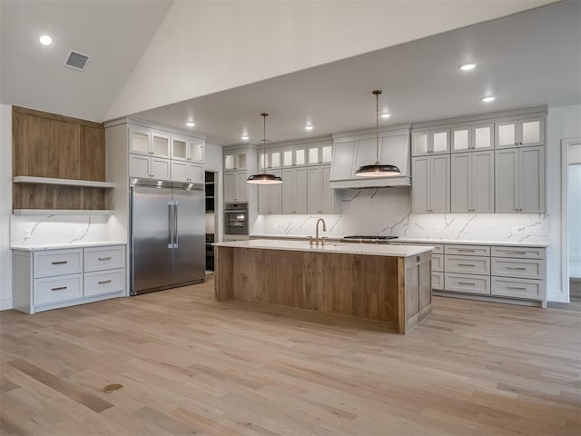 kitchen with appliances with stainless steel finishes, light wood finished floors, tasteful backsplash, a kitchen island with sink, and recessed lighting