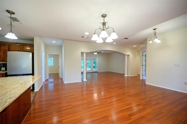 unfurnished living room featuring ornate columns, arched walkways, a chandelier, wood finished floors, and baseboards